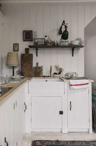 A white cottage style kitchen with original cabinets and open shelving above a sink