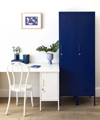 A set of three lockers (2 tall navy and one small white locker) in home office with white chair and desk