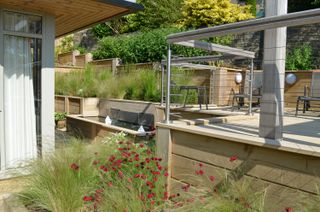 sloping garden ideas: raised patio area in a sloping garden with a water feature connecting two different levels