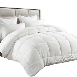 A white comforter on a bed with plush white pillows and a luxurious padded headboard