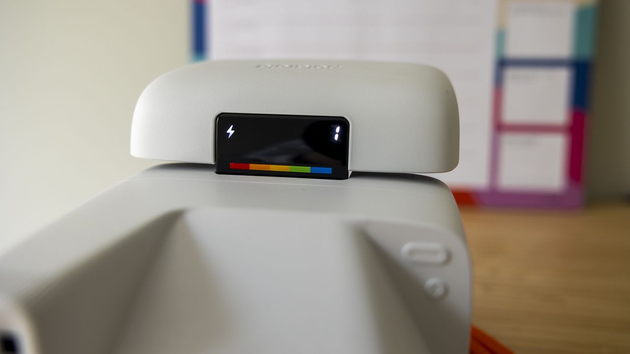 A white Polaroid Flip camera sits on a wooden desk