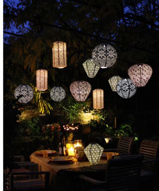 Romantic after dark garden scene with a variety of suspended lanterns above an intimate dining set-up.