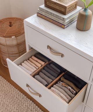 A white drawer with an open drawer with folded neutral materials in it