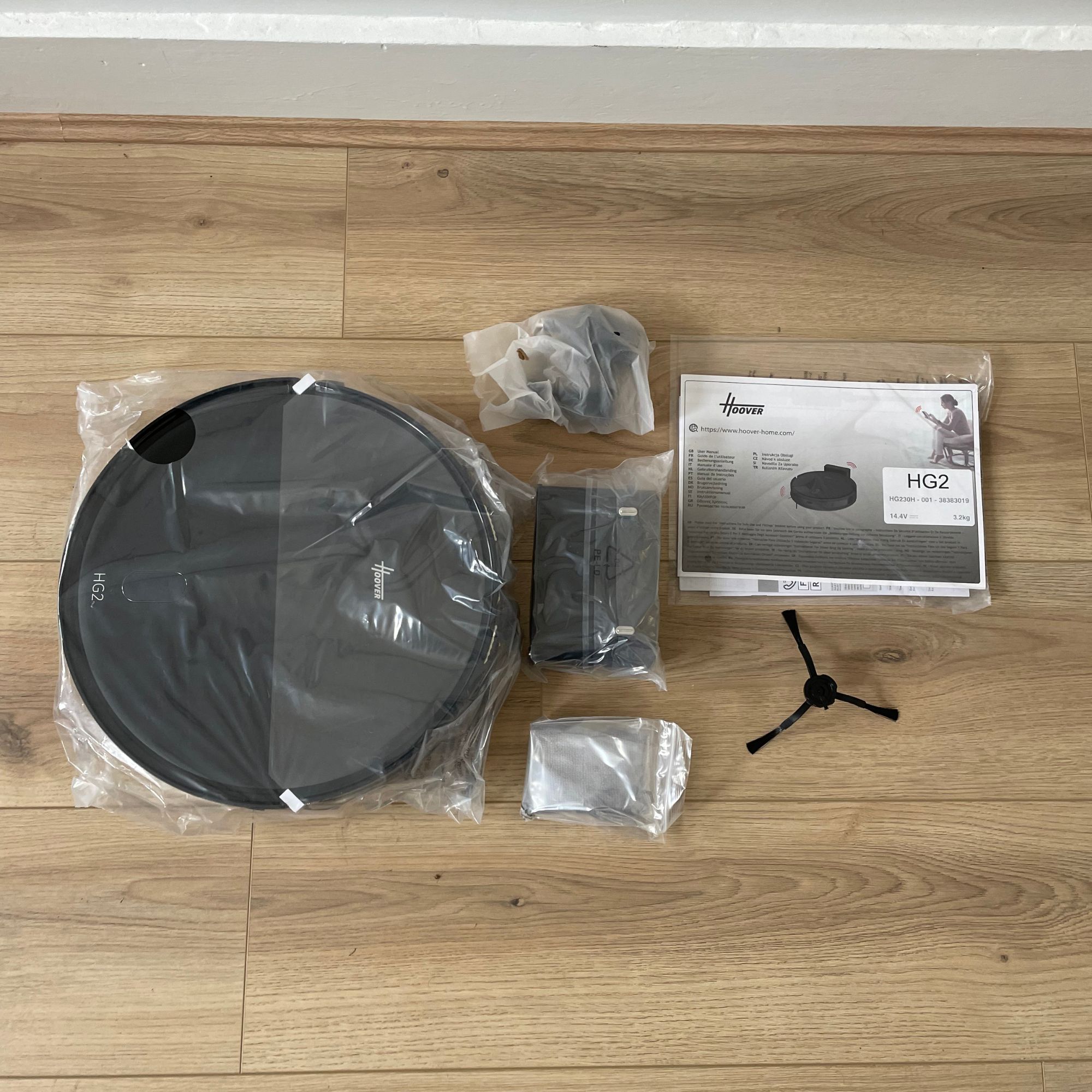Hoover HG2 robot vacuum and mop components wrapped in plastic and laid out on wood-effect flooring
