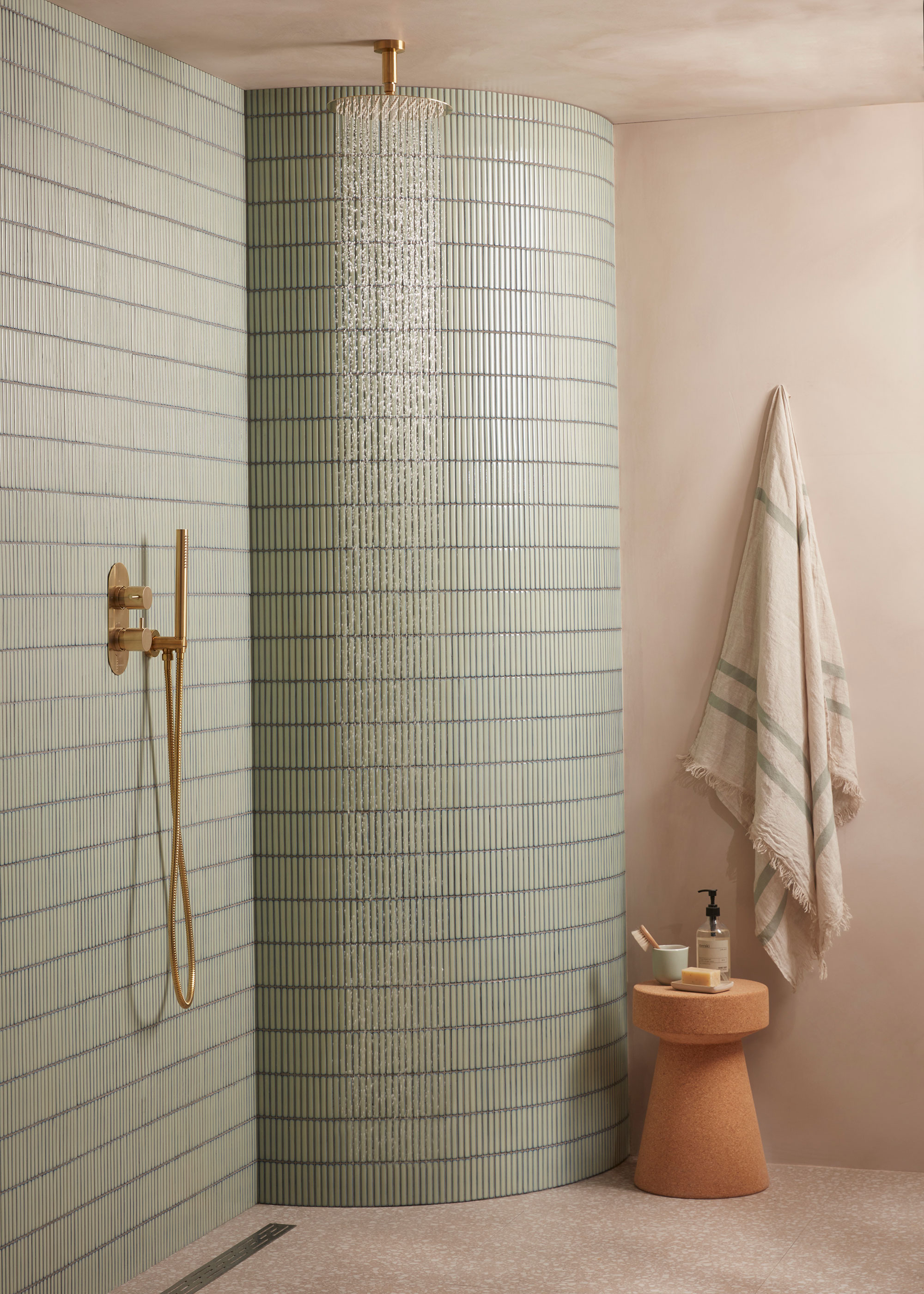 brass ceiling mounted shower head and brass handheld shower head in wet room with curved shower wall