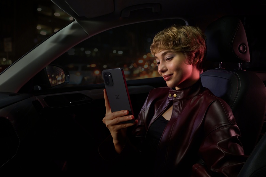 The OnePlus 15R in its black option in the hands of a model inside a vehicle.