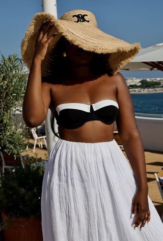 a close photo of a woman wearing the black-and-white swim trend with a white strapless bikini top styled with a white maxi skirt and a celine raffia hat