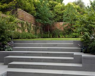 Design for a sloping garden using wide grey stone steps by Bowles & Wyer