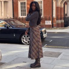 @_livmadeline wearing a brown check midi skirt with a cardigan and brown knee-high boots 