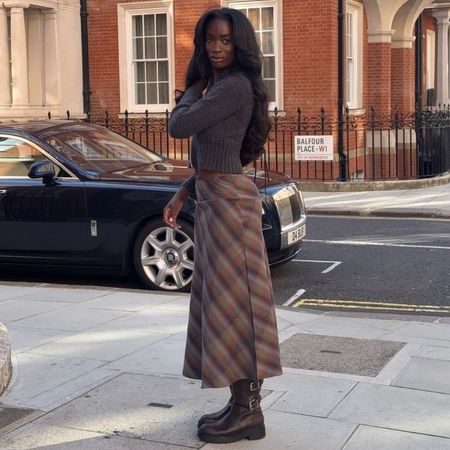 @_livmadeline wearing a brown check midi skirt with a cardigan and brown knee-high boots