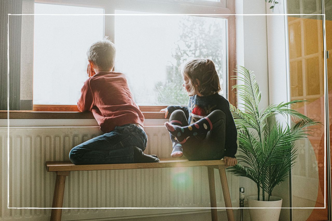 Young children sat on bench by radiator looking out of the window