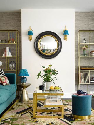 living room with white walls statement circle mirror with wall lights eitherside. Gold coffee table, statement rug and blue sofa and footstool
