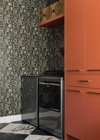 small laundry room with orange units and dark patterned wallpaper