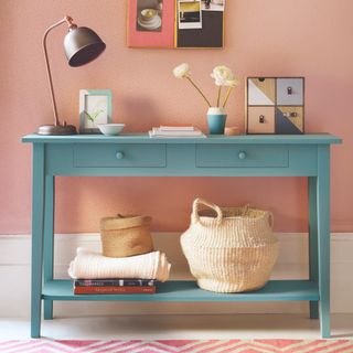 A hallway with a micro-patterned wallpaper and a blue storage console table with storage baskets