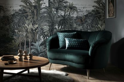 A dark green velvet couch for a small living room with jungle print wallpaper.