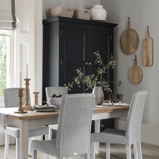 Neutral dining room with country style furniture and a tall black painted wardrobe used for storage