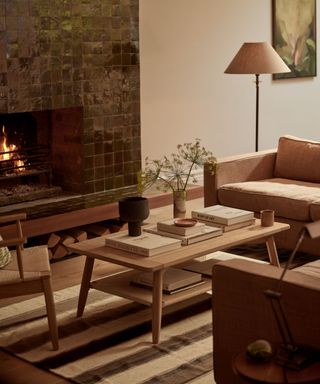 A wooden, two-tiered coffee table in a neutral living room with a green tiled fireplace