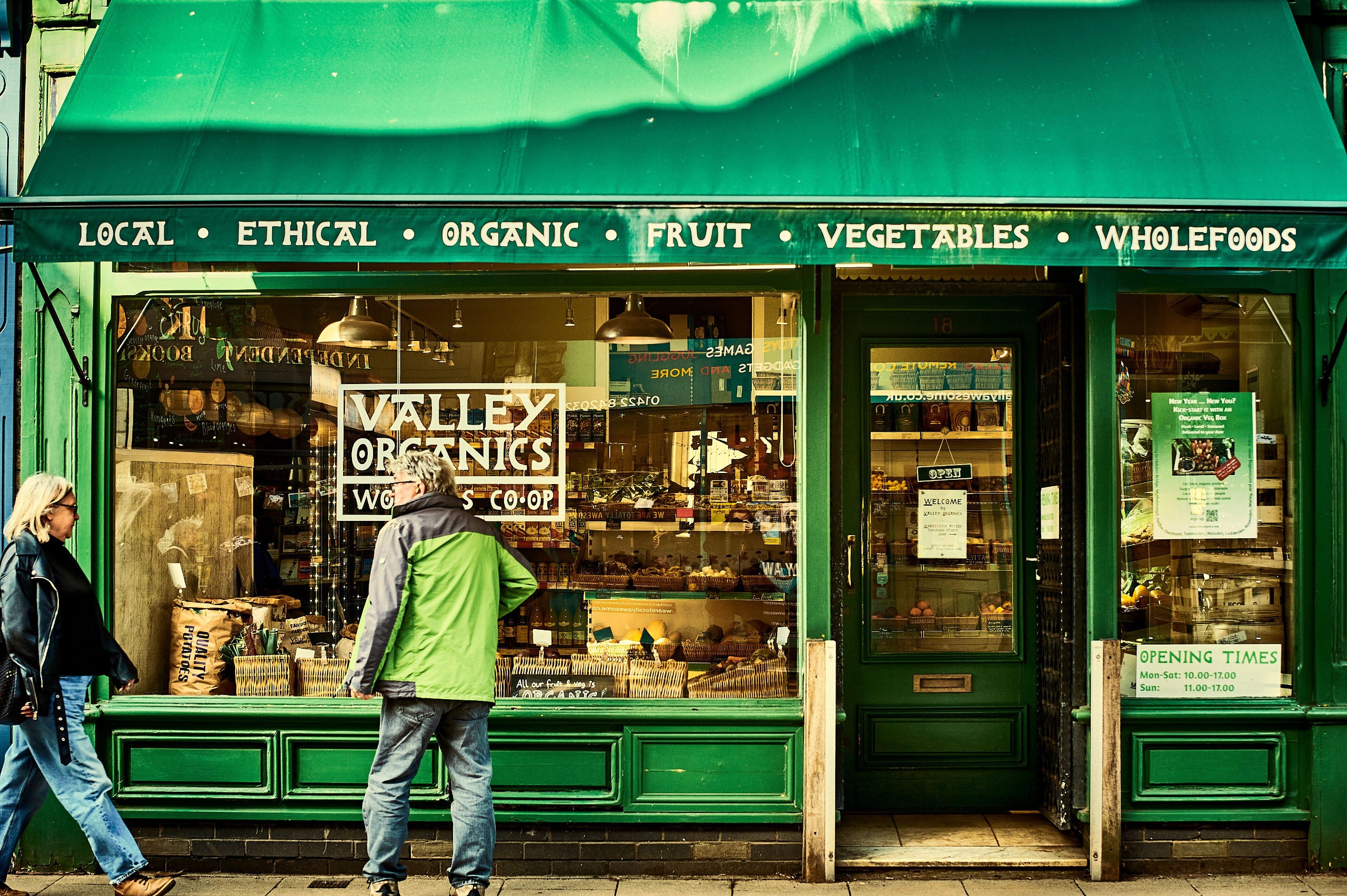 Two people walk past a green shop front that sells organic goods