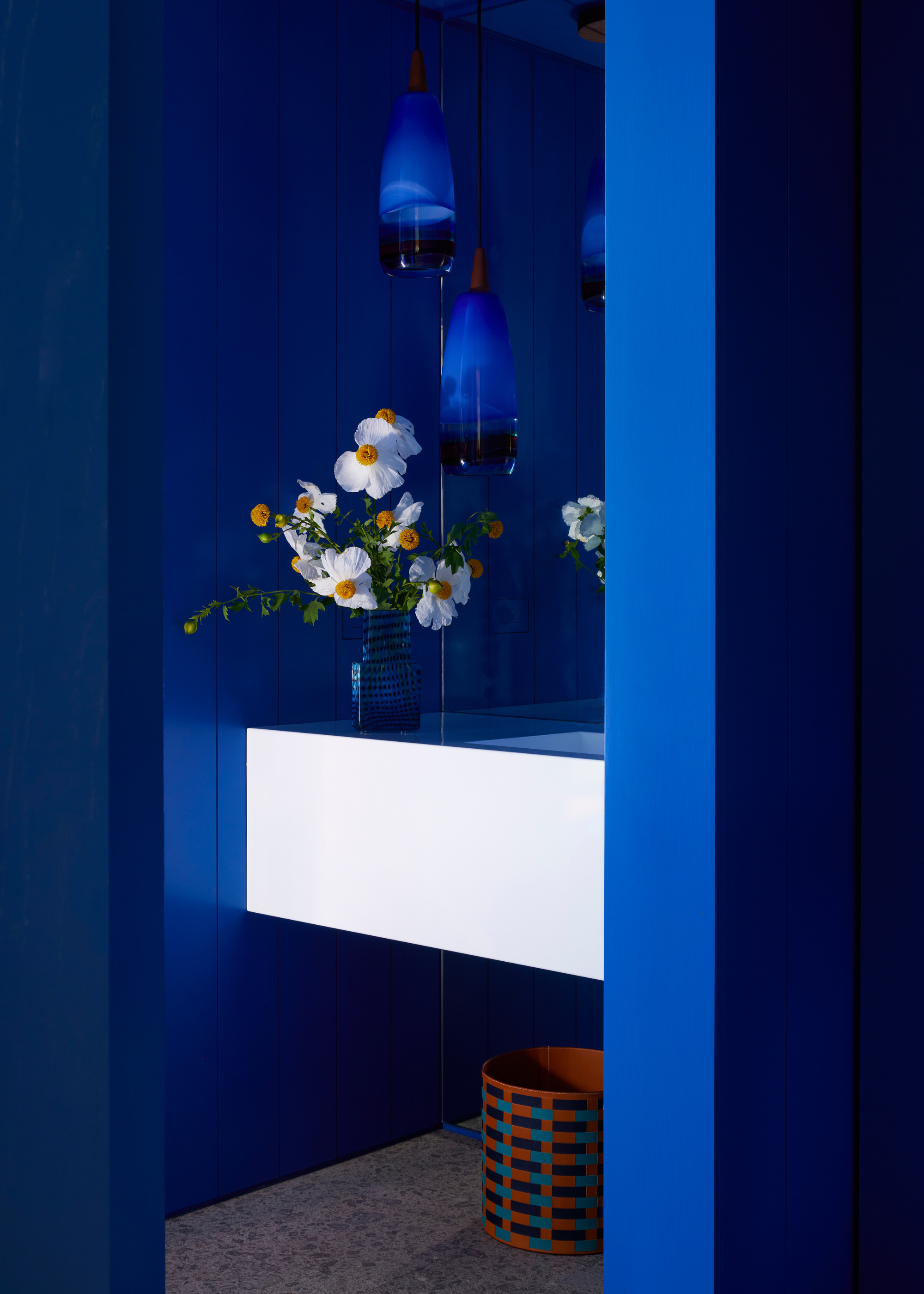 A powder room decorating with a bold cobalt blue with a bright white sink and white flower arrangement providing a stark contrast