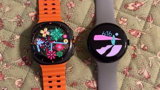 The Google Pixel Watch 3 sitting beside the Samsung Galaxy Watch Ultra on a floral-pattern tablecloth, both with brightly colored watch faces.