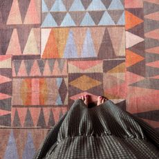 Point of view of woman looking down onto feet while standing on rug with abstract pattern in oranges, browns, pinks and blues