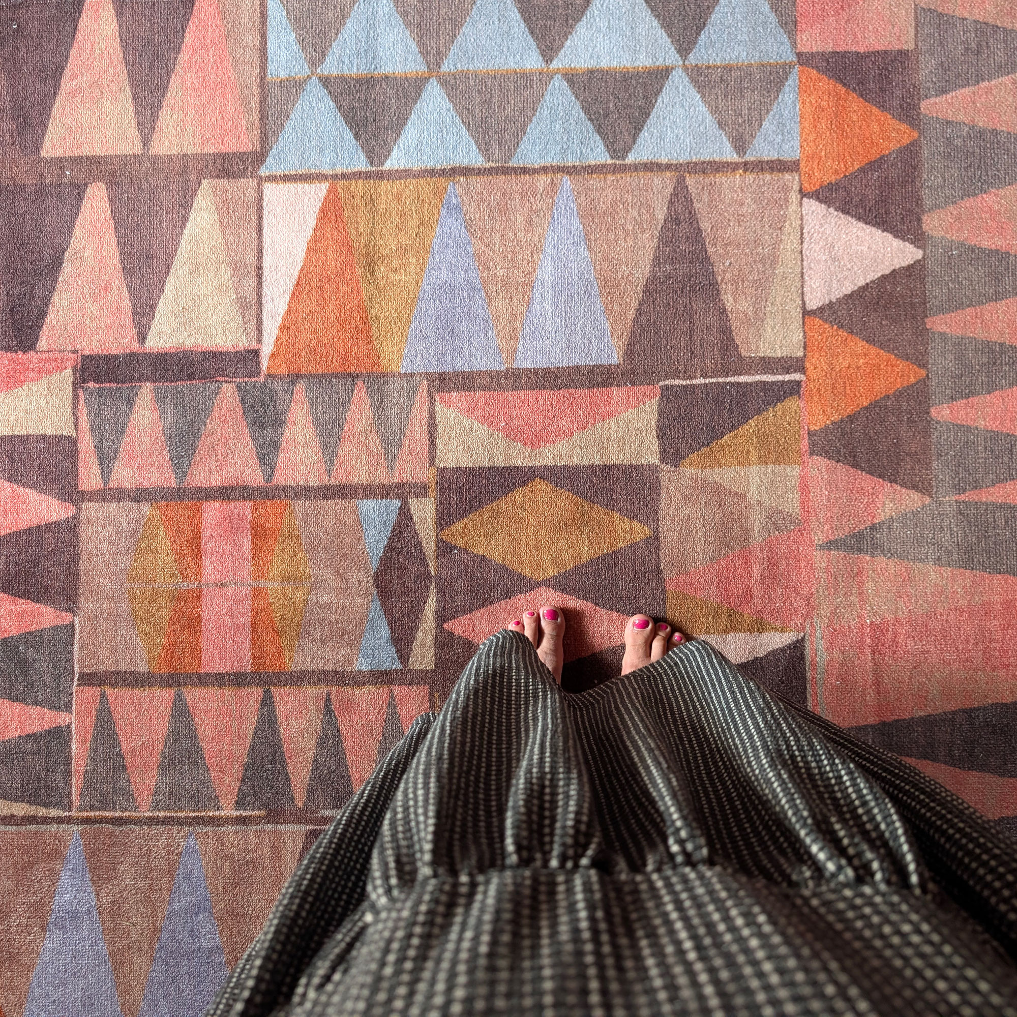 Point of view of woman looking down onto feet while standing on rug with abstract pattern in oranges, browns, pinks and blues