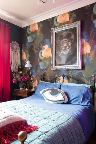 A guest bedroom with floral paint effect patterned wallpaper, metal bed, and a framed photograph above