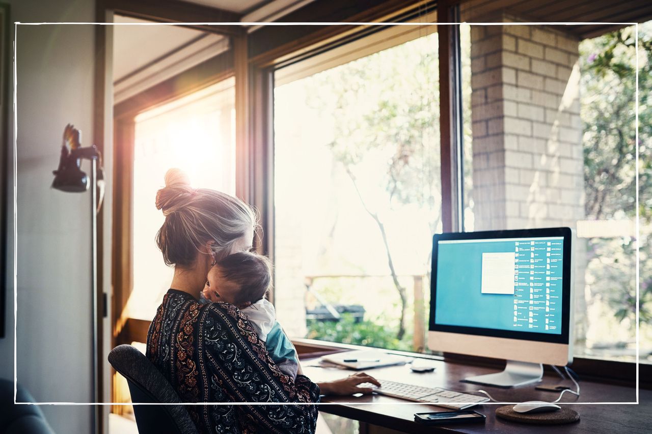 new mum holding baby while sat at a desk looking at a computer screen