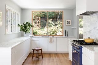 A kitchen with large picture window, white lower units and a blue La Canche range