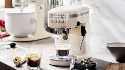 White kitchenaid espresso machine on a countertop with coffee and a stand mixer in the background