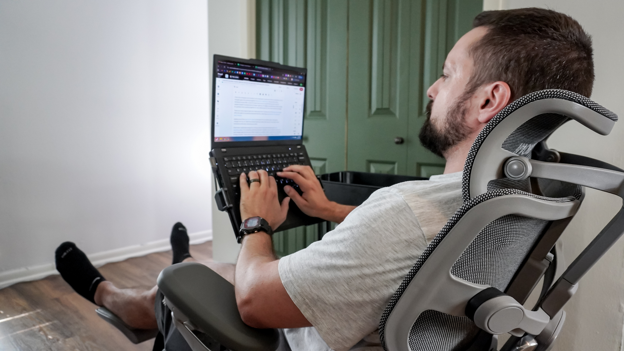 A person working on a laptop at a DIY rollable workstation in an office chair with their feet up