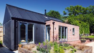 Contemporary annexe clad in timber and metal, with a large raised garden, and trees in the background