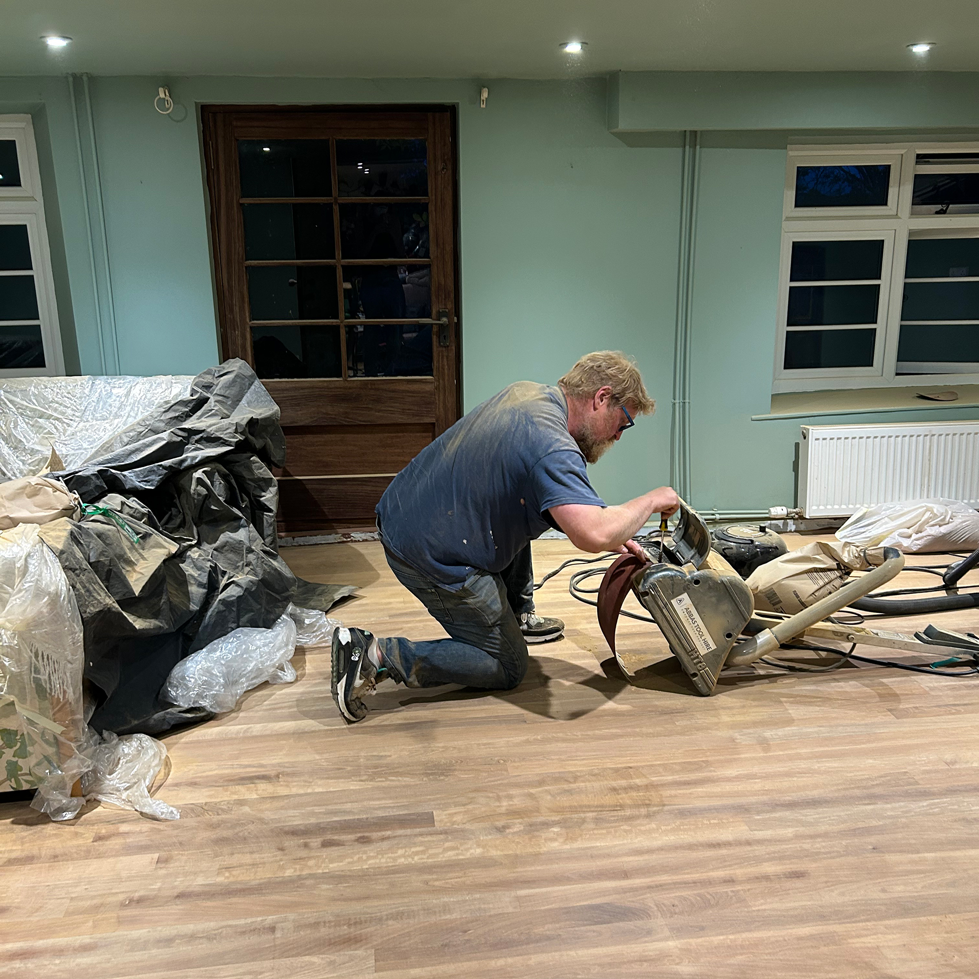 Man kneeling on wooden floor looking at sander