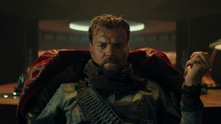 a brooding man sits in a high-backed chair thinking