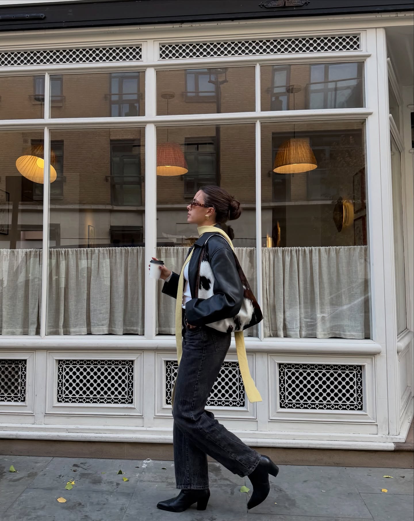 Fashion person Tia Dewitt wears a Gen Z spring outfit idea. She wears black straight leg jeans, a leather fitted biker jacket cowboy boots and carries a cowprint bag. This image was taken from her Instagram recently.