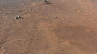 nasa's perseverance rover is seen from the air against the red dirt and scattered boulders