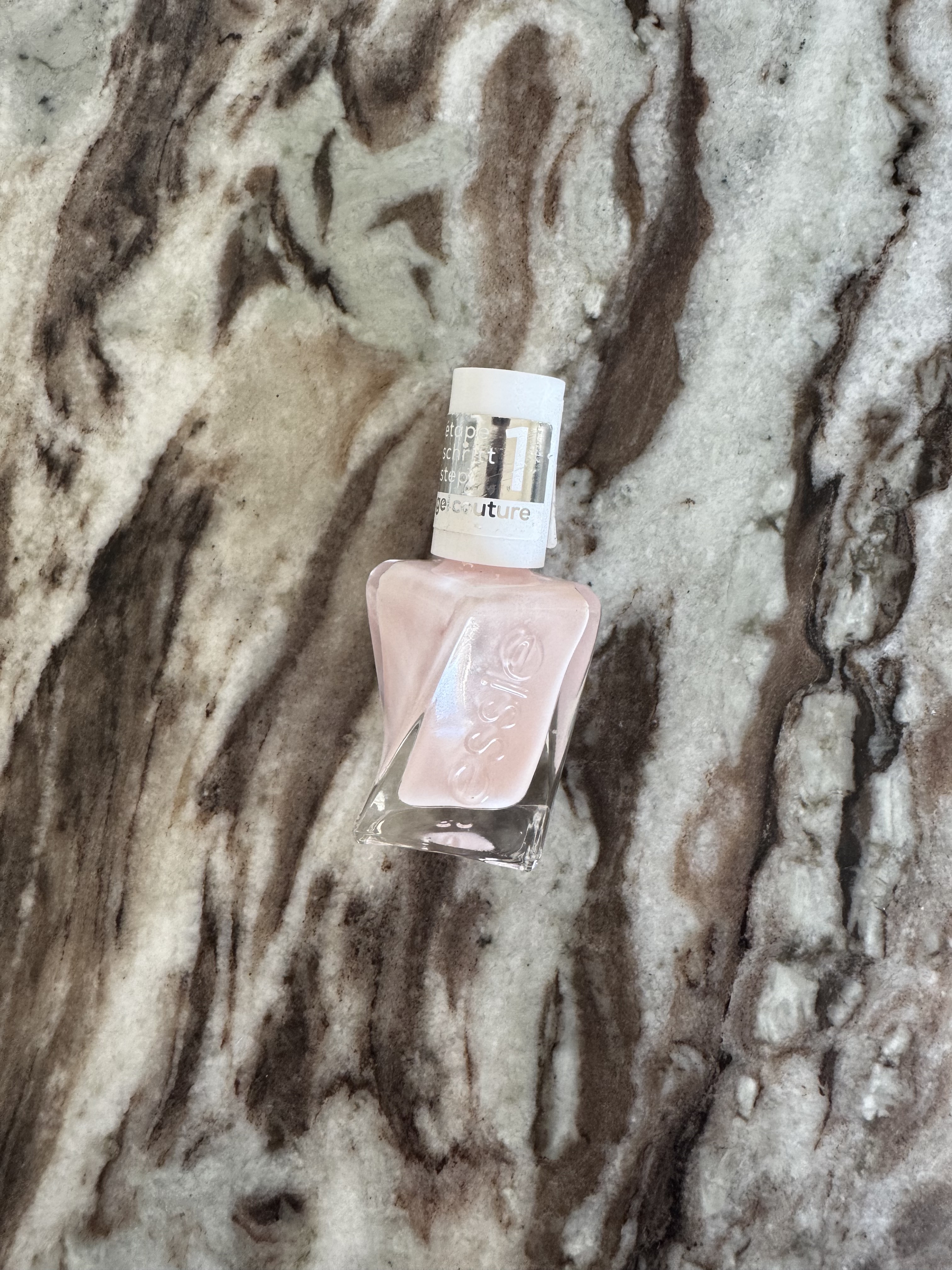 A bottle of Essie Gel Couture nail polish in the shade Fairy Tailor, which is a sheer milky pink