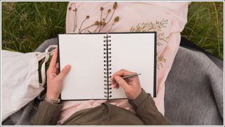 Woman sitting on a meadow writing down something in her notebook, partial view