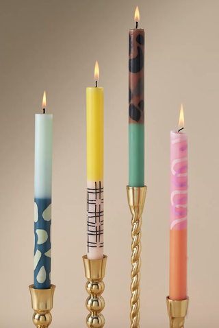 four tapered candles of varying colors and prints sit in twisted gold candlesticks