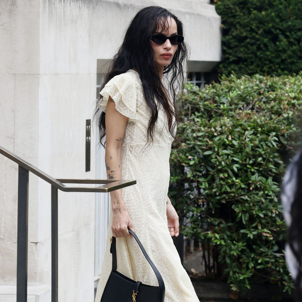 Zoe Kravitz walks down steps outside wearing a butter yellow dress with black ballet flats and a YSL handbag.