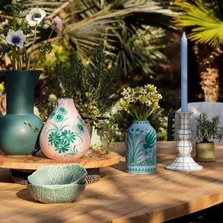 Vaisselle ceramic vases on a wooden outdoor table next to candlesticks.