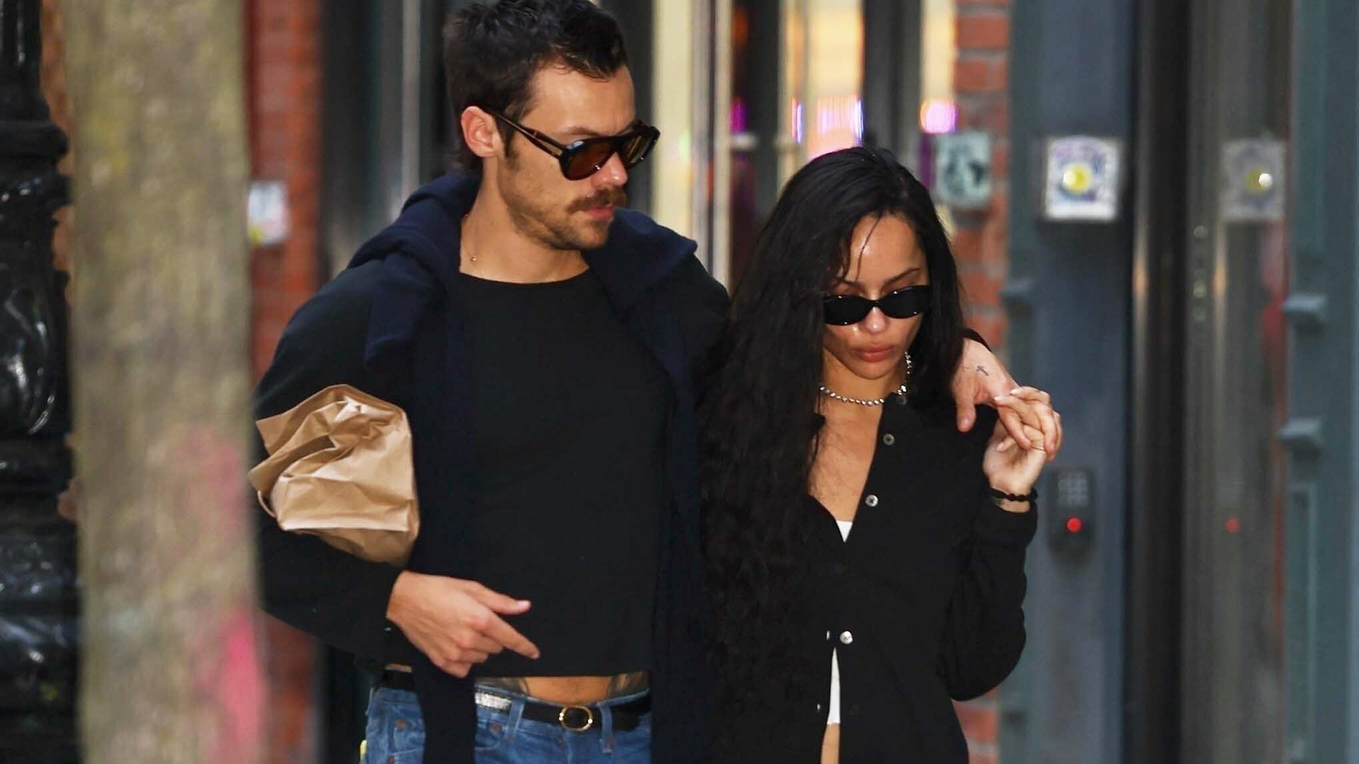 Zoe Kravitz and Harry Styles walking in NYC wearing black tops and jeans.