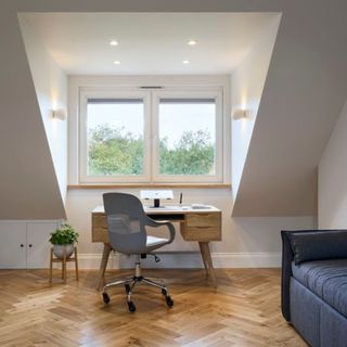 Interior view of loft with dormer window with desk and chair, sofa to one side and wood floor