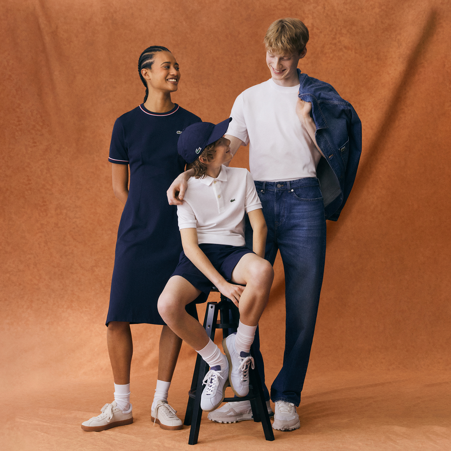 2 people standing and child on a stool in lacoste clothes against a plaster background