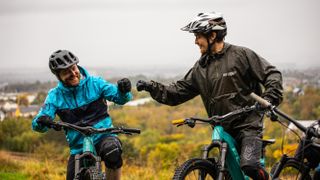 Two mountain bikers fist bump at the top of a hill
