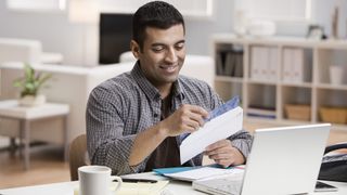 Man opening an envelope while sitting in front of laptop.