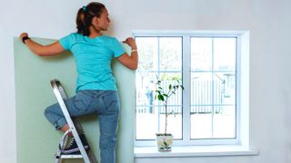 Women in blue putting up wallpaper next to window