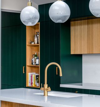 A brass mixer tap mounted on a white counter top with dark green kitchen cabinets seen in the background
