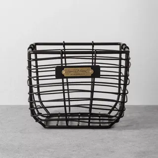 A black wire storage basket with a brass label tag on the front. 