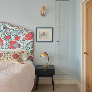 colour ideas for cottagecore decor, blue bedroom with upholstered headboard, decorative cushion, black side table, artwork, wall light, built in cupboard
